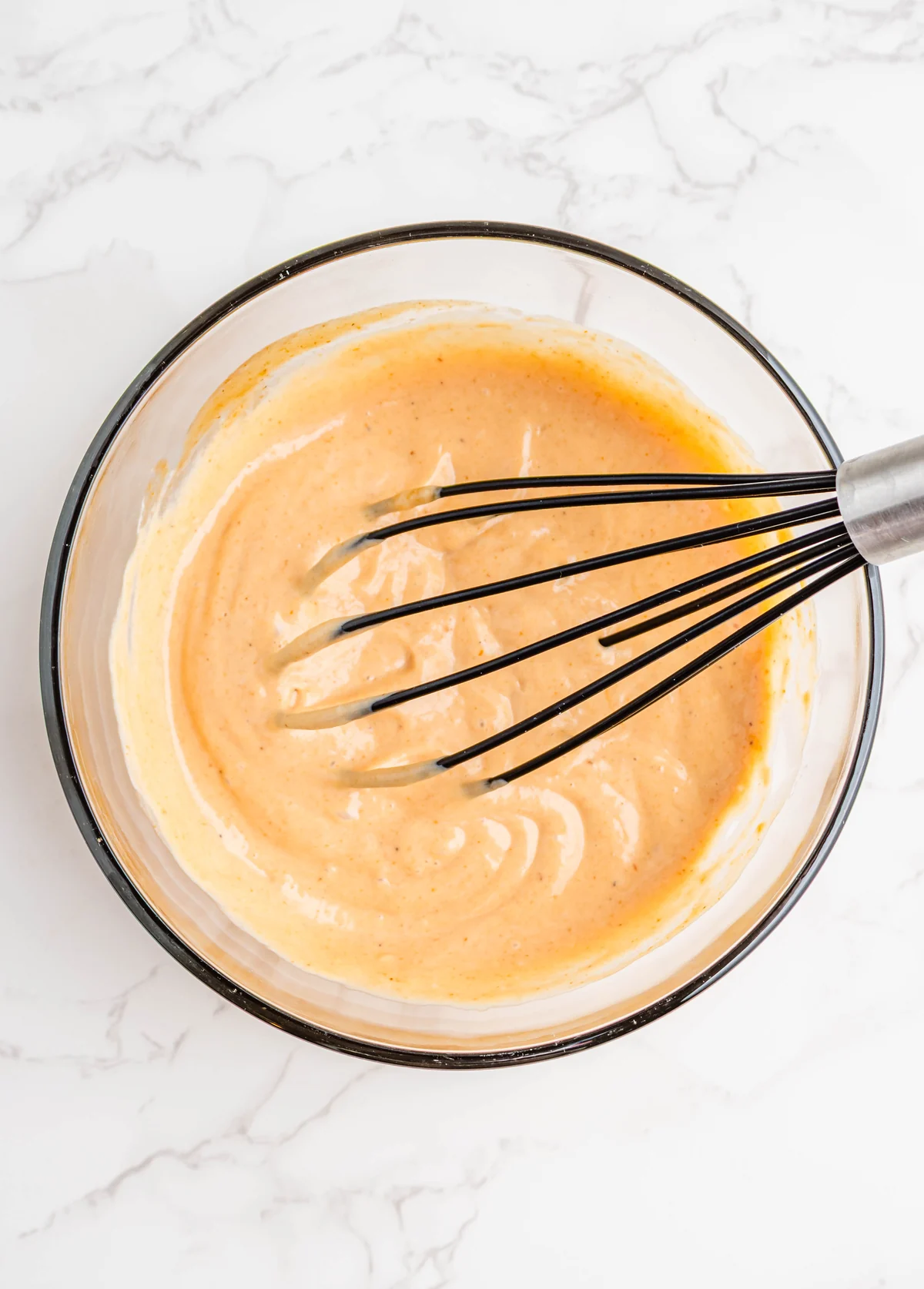 Smooth orange campfire sauce mixed in a glass bowl with a whisk.