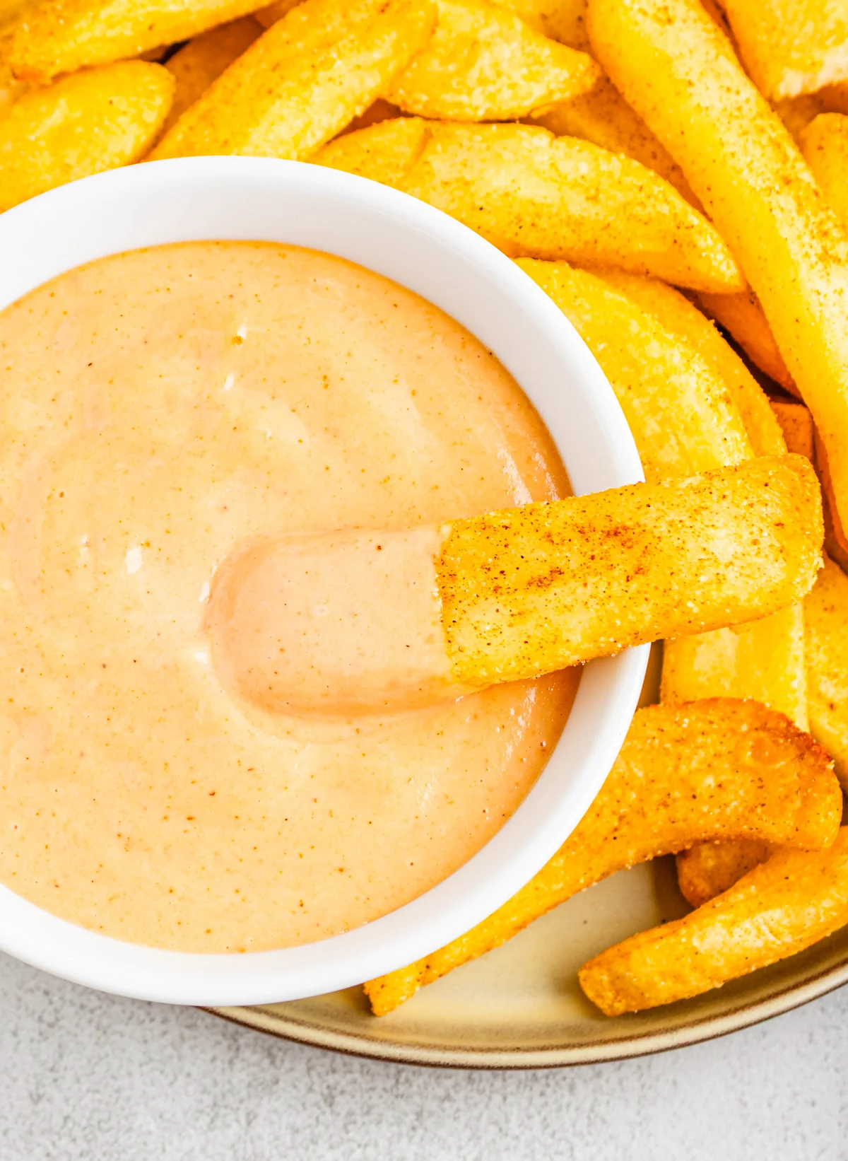 Overhead closeup of a fry dipped into campfire sauce with fries around the bowl.