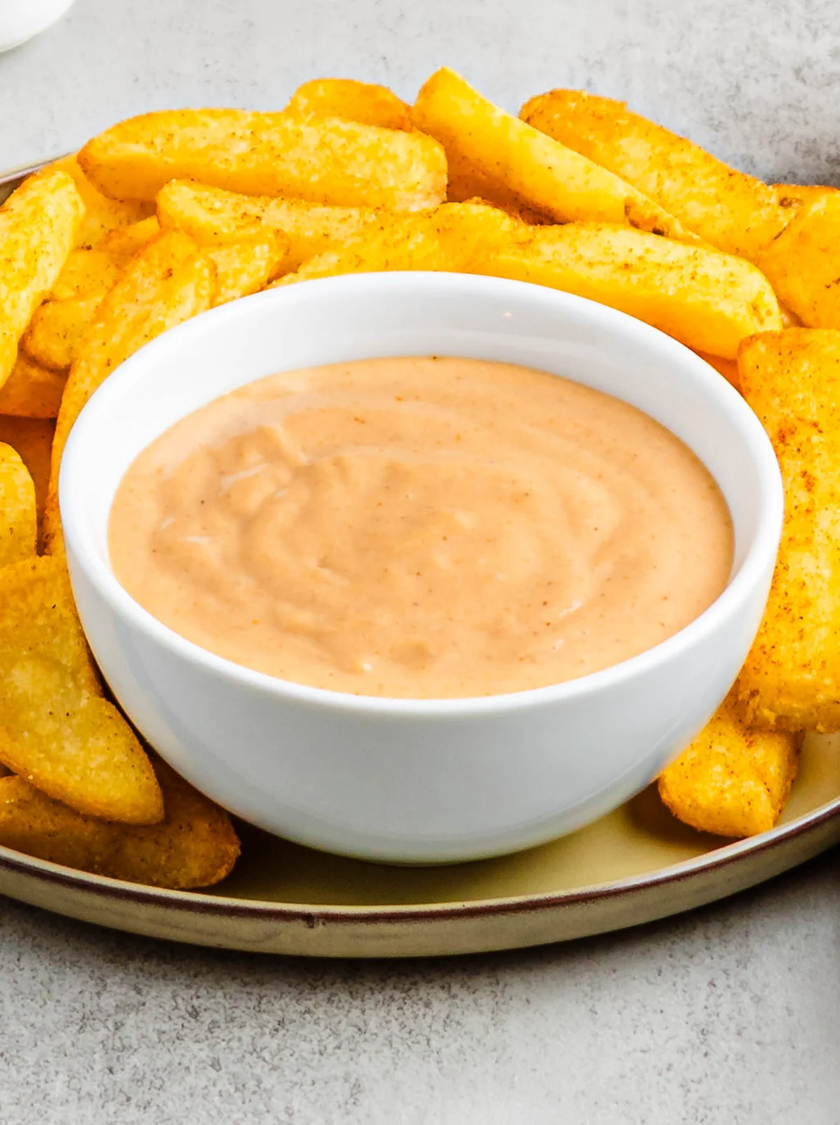 A white bowl of campfire sauce served with a platter of seasoned fries.