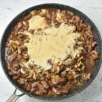 Sour cream mixture added to venison and mushrooms in a skillet