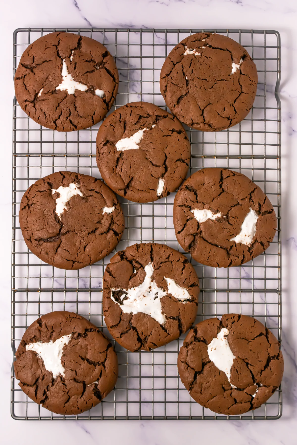 Baked chocolate cookies with marshmallow centers cooling on a wire rack.