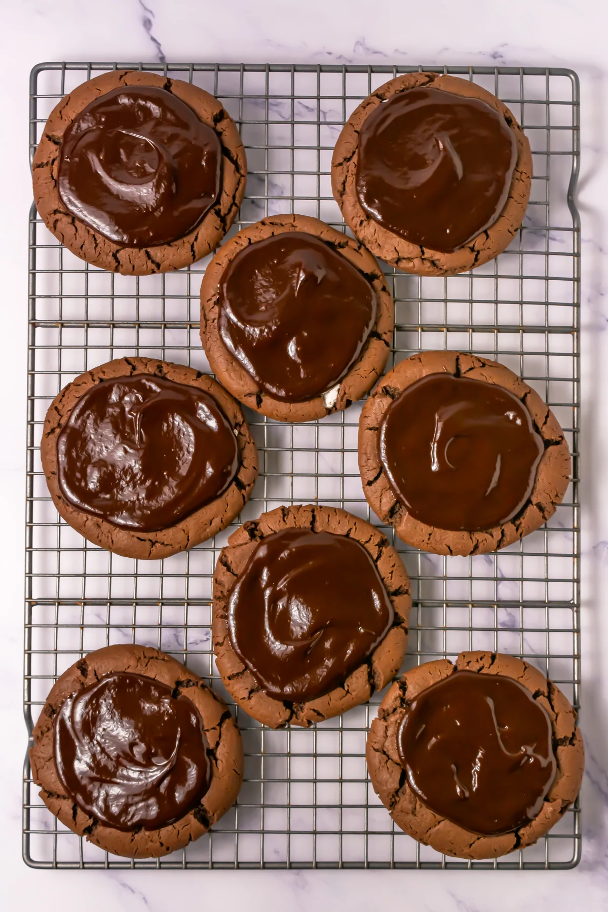 Chocolate marshmallow cookies topped with glossy chocolate ganache on a cooling rack.