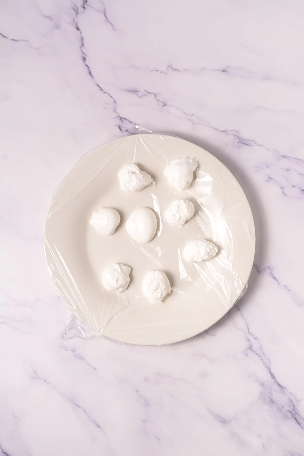 Small portions of marshmallow fluff on a plate covered with plastic wrap.