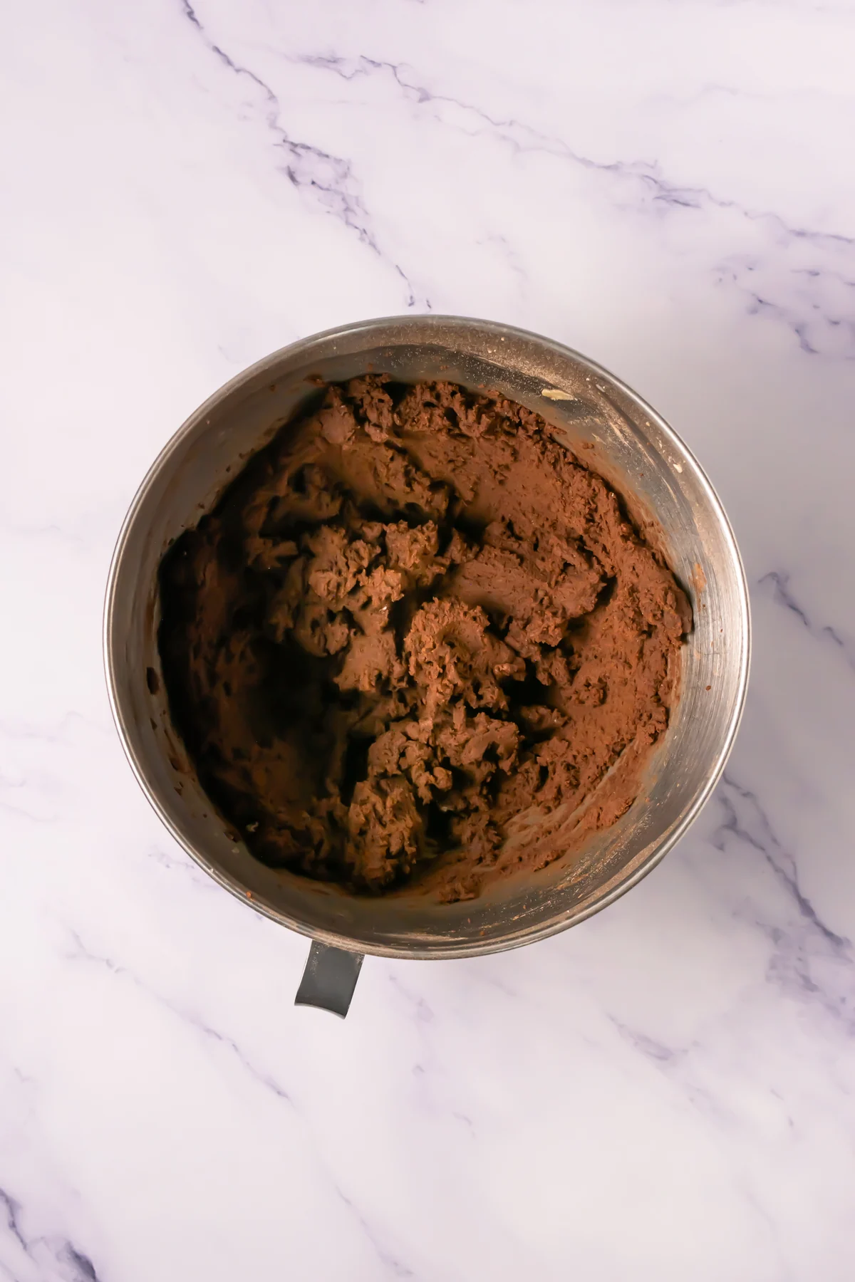 Thick chocolate cookie dough in a metal mixing bowl.