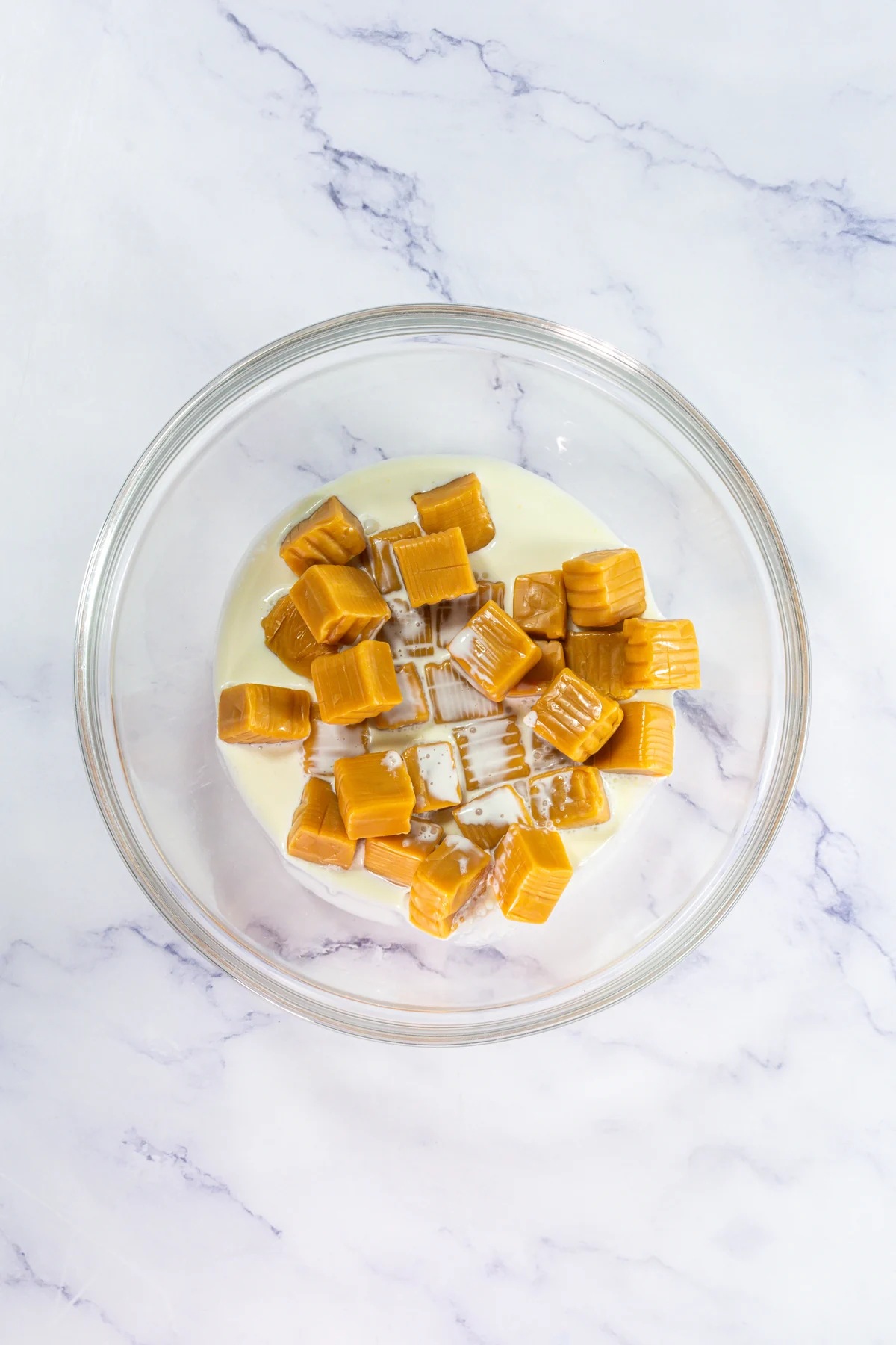Crumbl Copycat Twix Cookies With Caramel and Toffee Caramel candies and heavy cream ready to melt in a glass bowl.