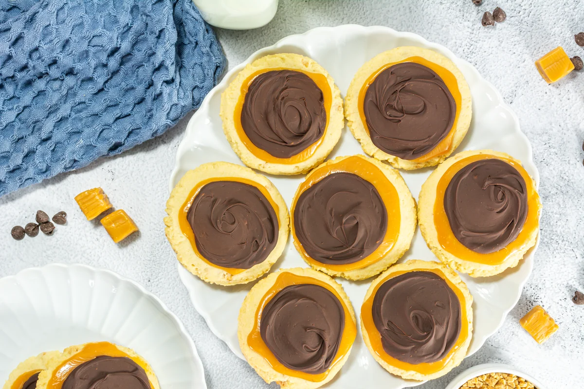 Plate of oversized caramel and chocolate topped cookies with a broken cookie in front.