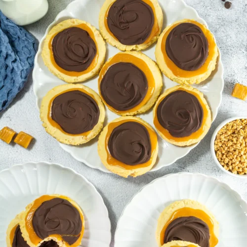 Crumbl Copycat Twix Cookies With Caramel and Toffee Soft copycat Twix Crumbl cookies with caramel and melted chocolate on a serving plate.