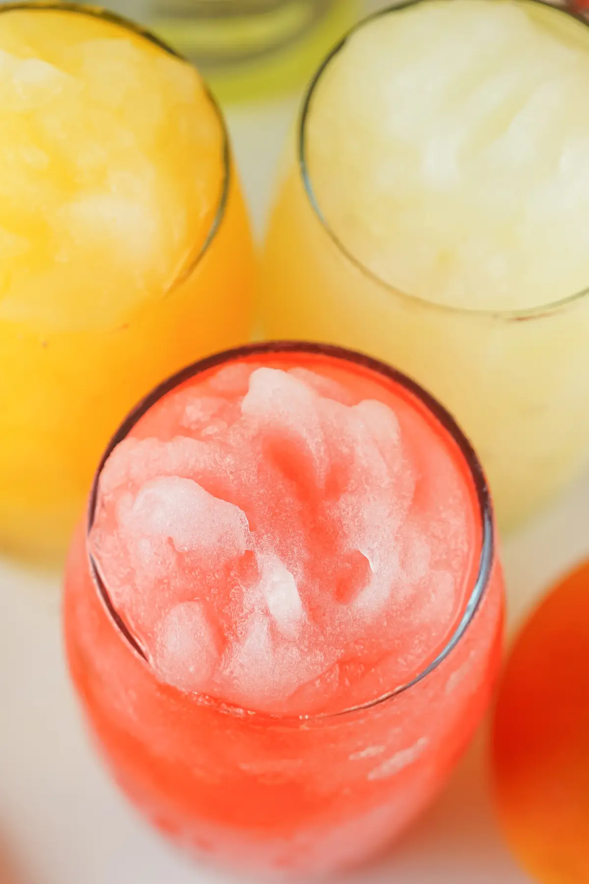 Close-up of three colorful frozen slushies in glasses—red, yellow, and pale—refreshing summer drinks