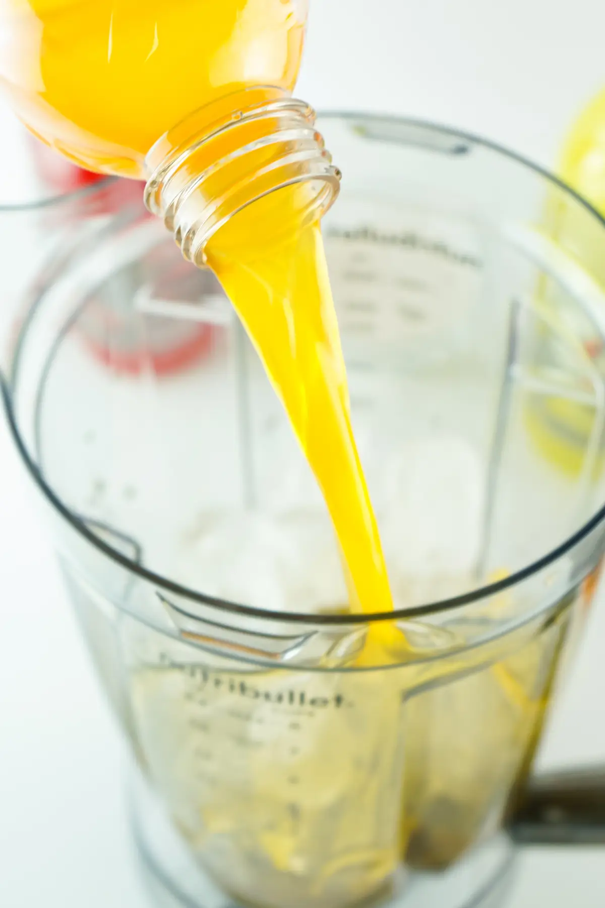 Close-up of orange juice being poured into a blender cup over ice to make a refreshing smoothie.