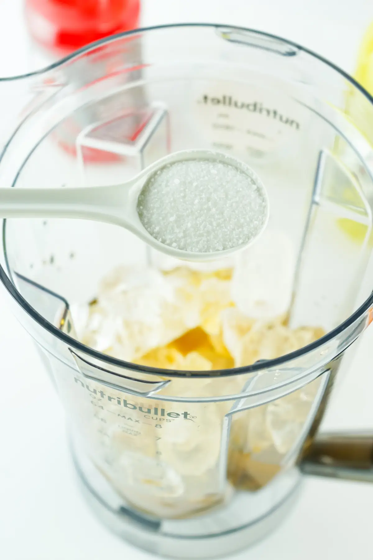 Spoonful of granulated sugar added to ice in a Nutribullet blender pitcher