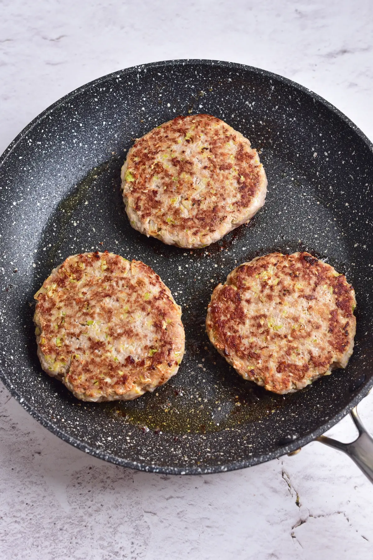 Ground chicken burger patties browned in a skillet