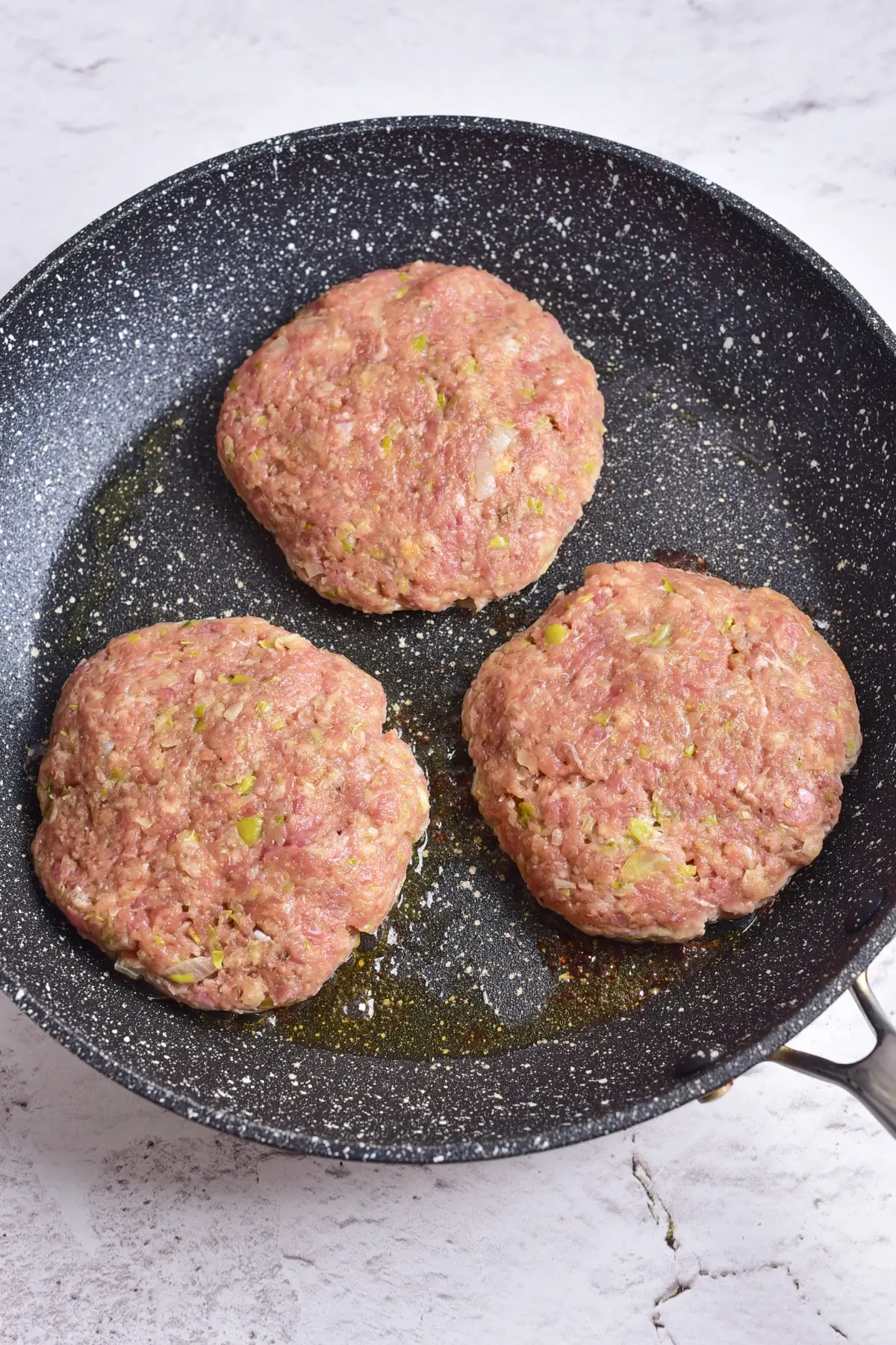 Raw ground chicken patties in a skillet before cooking