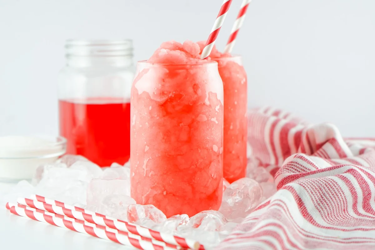Hawaiian Punch slushies served with striped straws, ice, and a jar of punch.