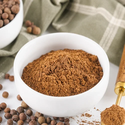 How to Make Ground Allspice From Whole Berries Ground allspice in a white bowl with whole allspice berries.