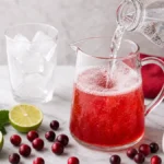 Sparkling water being poured into cranberry lime mocktail mixture in a glass pitcher.