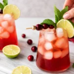 A cranberry lime mocktail being garnished with fresh lime and mint.