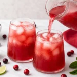 Cranberry lime mocktail being poured from a pitcher into ice-filled glasses.