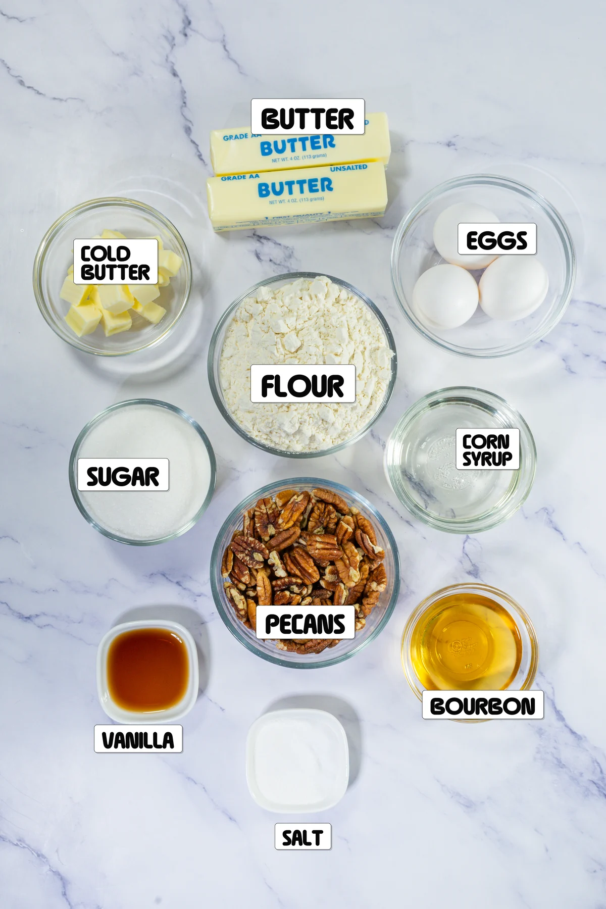 Ingredients for bourbon pecan pie labeled on a marble surface.