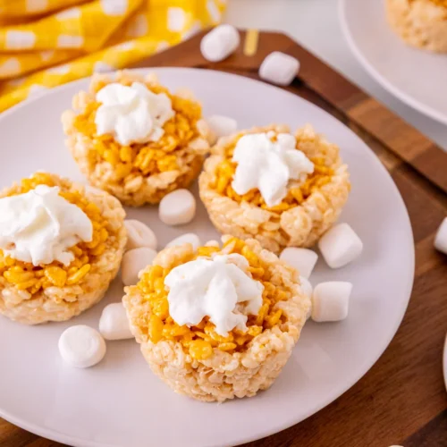 Mini pumpkin pie Rice Krispie treats with whipped topping on a white plate.