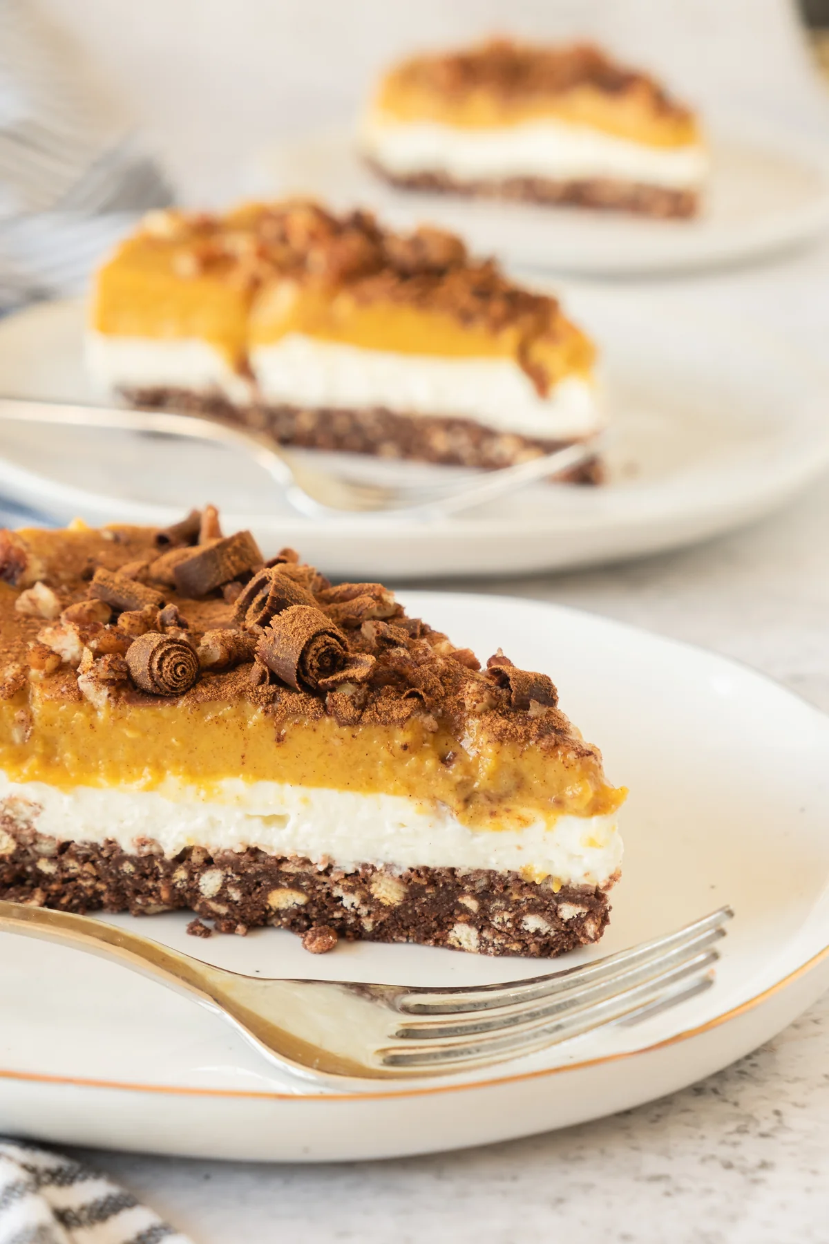 Close-up of a layered pumpkin cheesecake slice with chocolate biscuit crust and cinnamon pumpkin topping.