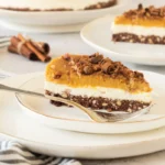 A slice of layered no bake pumpkin cheesecake on a white plate.