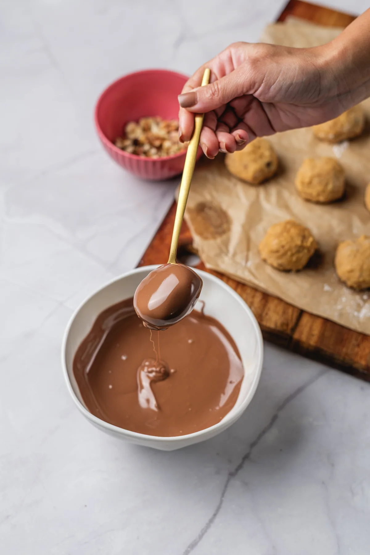 Peanut butter ball dipped in melted chocolate with shaped balls in the background.