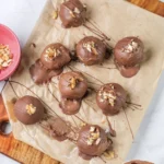 Finished chocolate covered peanut butter balls topped with chopped nuts on parchment paper.