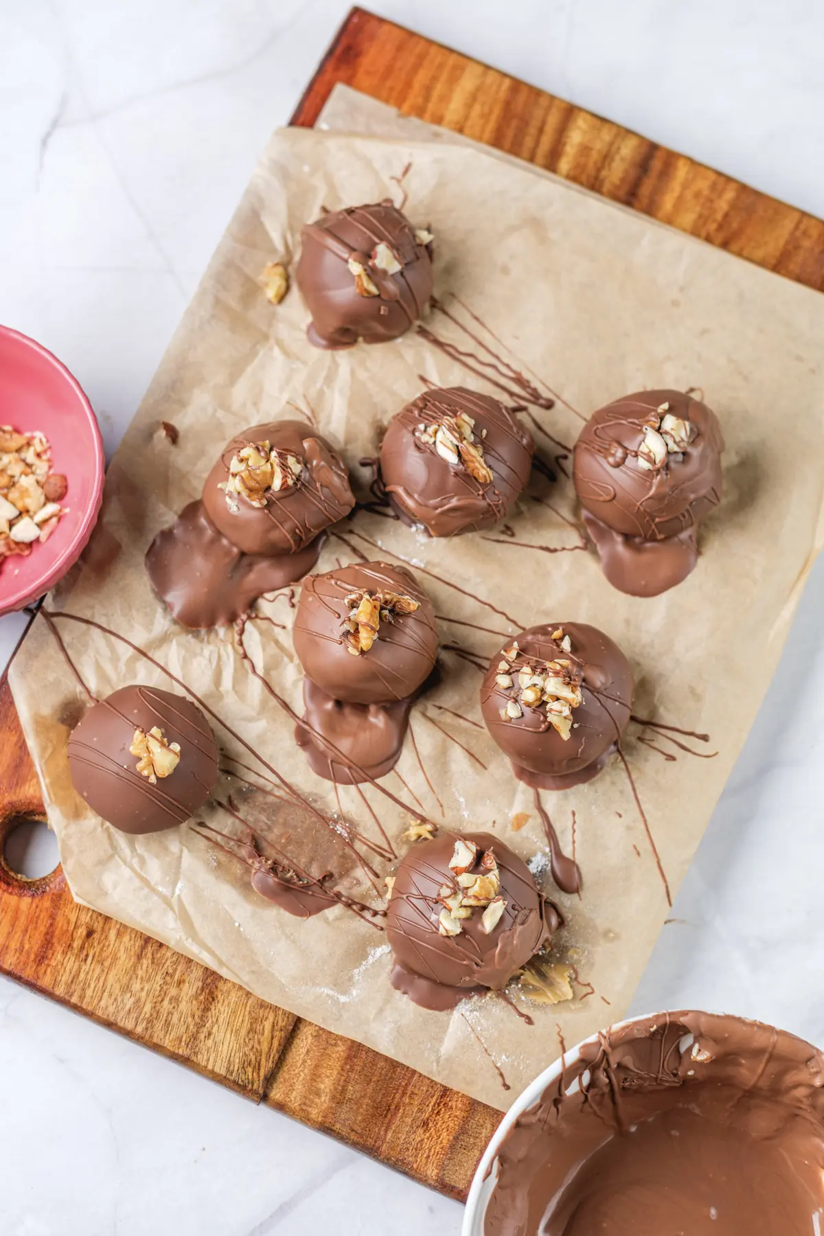 Finished chocolate covered peanut butter balls topped with chopped nuts on parchment paper.