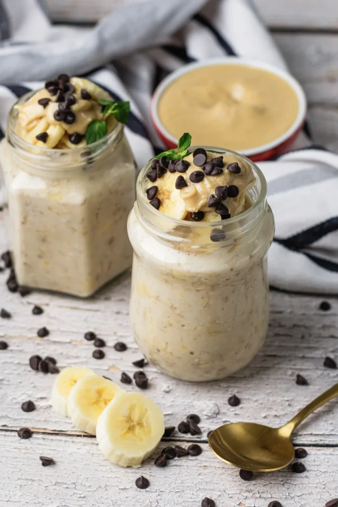 Creamy peanut butter banana overnight oats in jars with banana slices, chocolate chips, and peanut butter.