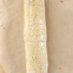 Plastic-wrapped pecan shortbread dough log on parchment paper before slicing.