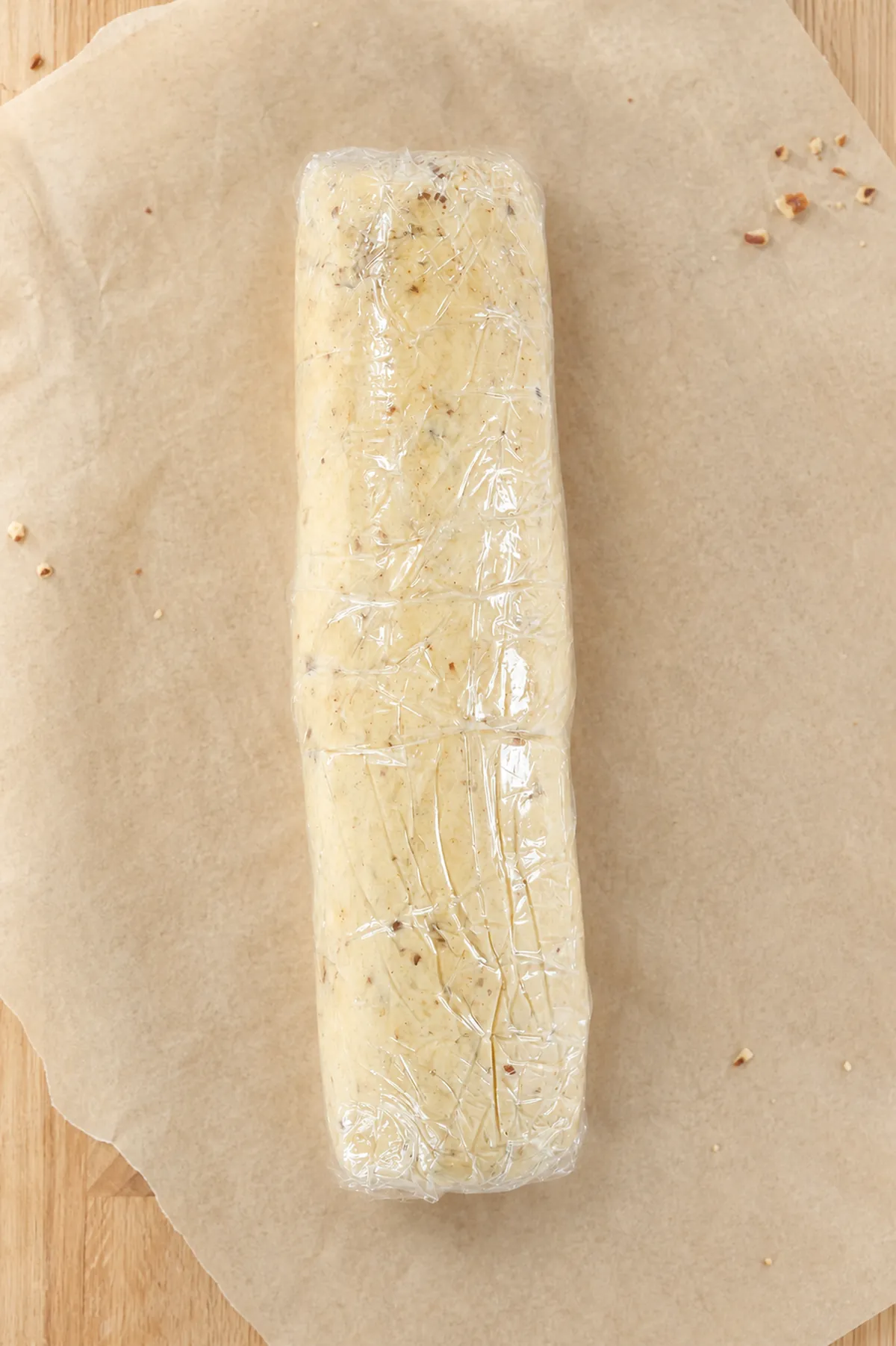 Plastic-wrapped pecan shortbread dough log on parchment paper before slicing.