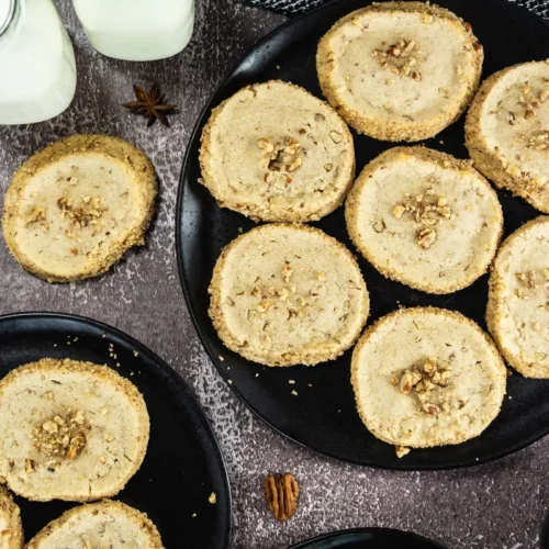 Pecan shortbread cookies arranged on black plates with milk bottles and pecans.