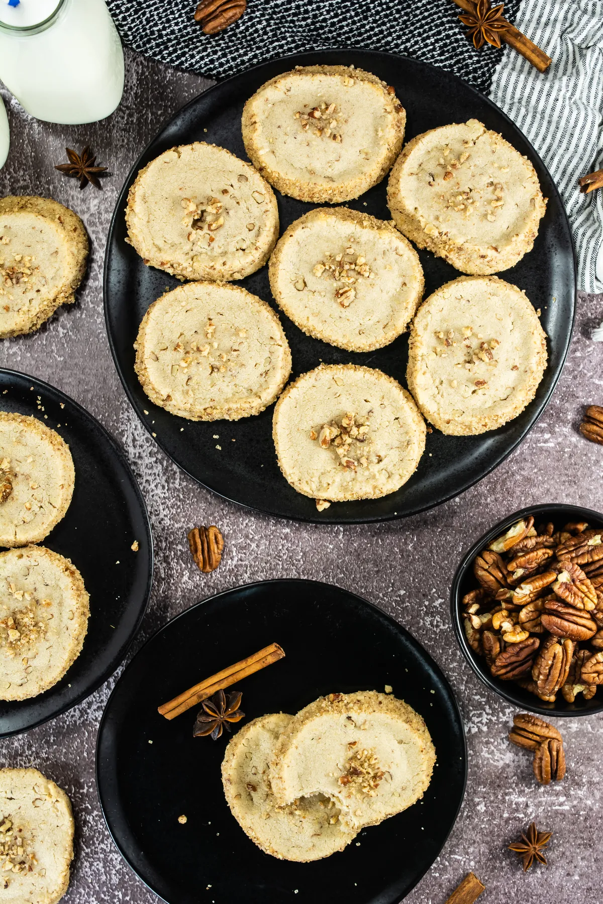 Overhead view of pecan shortbread cookies on black plates with cinnamon sticks and pecans.