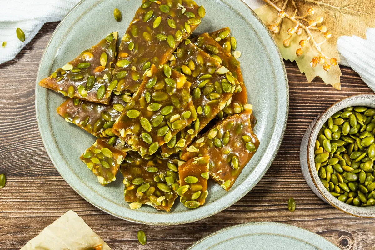 Pumpkin seed brittle pieces on a green plate with extra pepitas nearby.