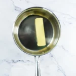 Unsalted butter melting in a stainless steel saucepan.