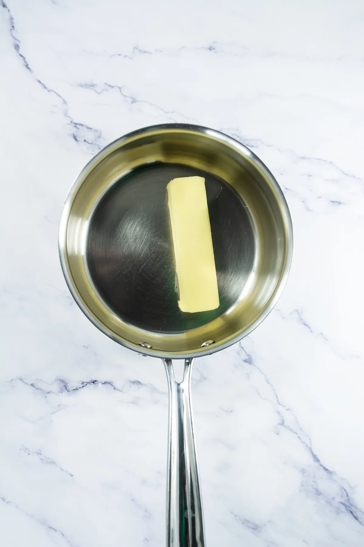 Unsalted butter melting in a stainless steel saucepan.