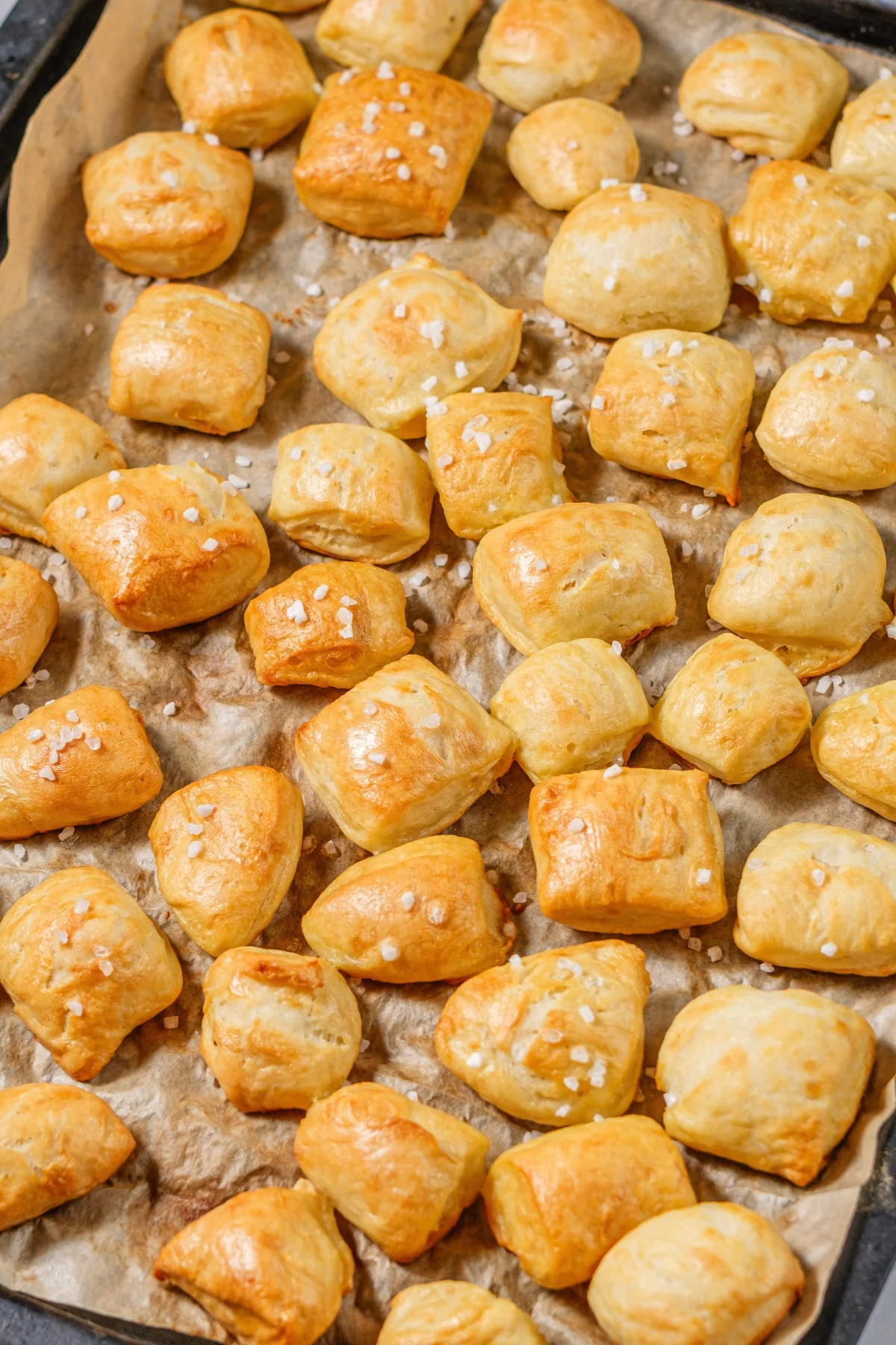 Golden pretzel bites with coarse salt on a parchment-lined baking sheet.