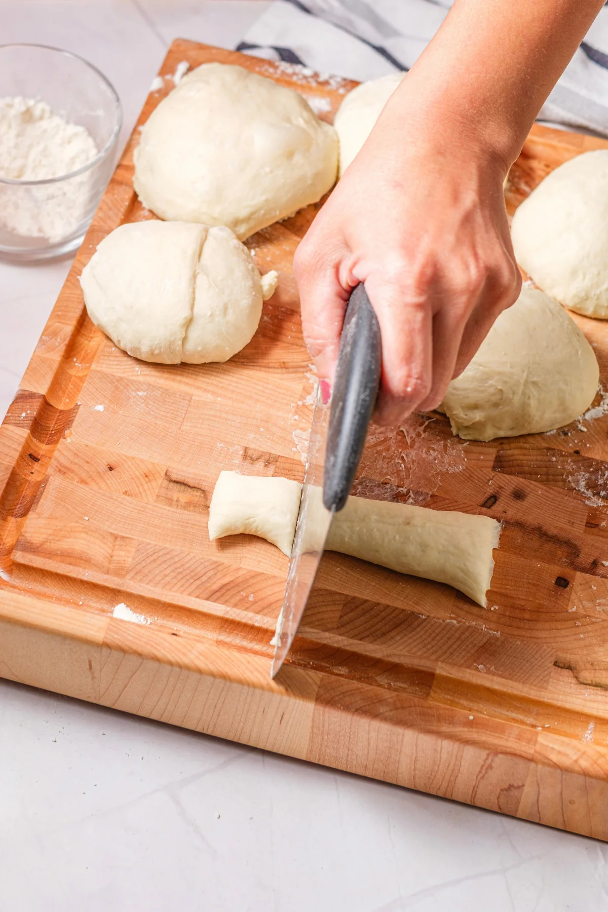 Pretzel dough rope being cut into bite-sized pieces on a wooden board.