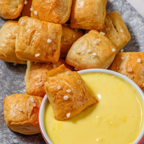 Golden homemade pretzel bites with coarse salt beside warm cheese dip.
