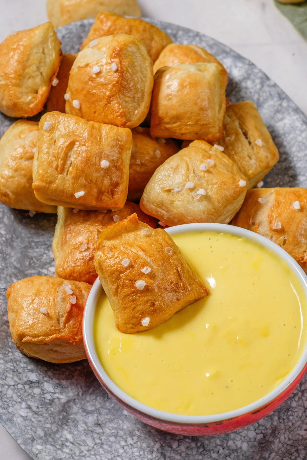 Golden homemade pretzel bites with coarse salt beside warm cheese dip.