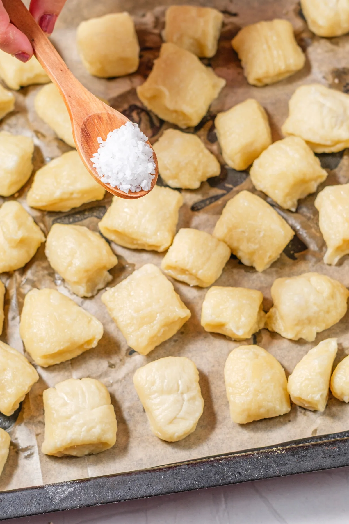 Coarse salt being sprinkled over pretzel bites on a parchment-lined baking sheet.