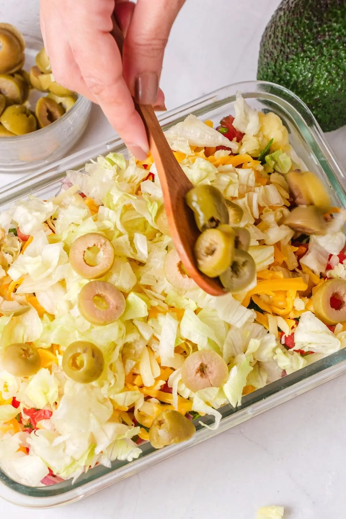 Adding olives to layered dip with cheese and lettuce