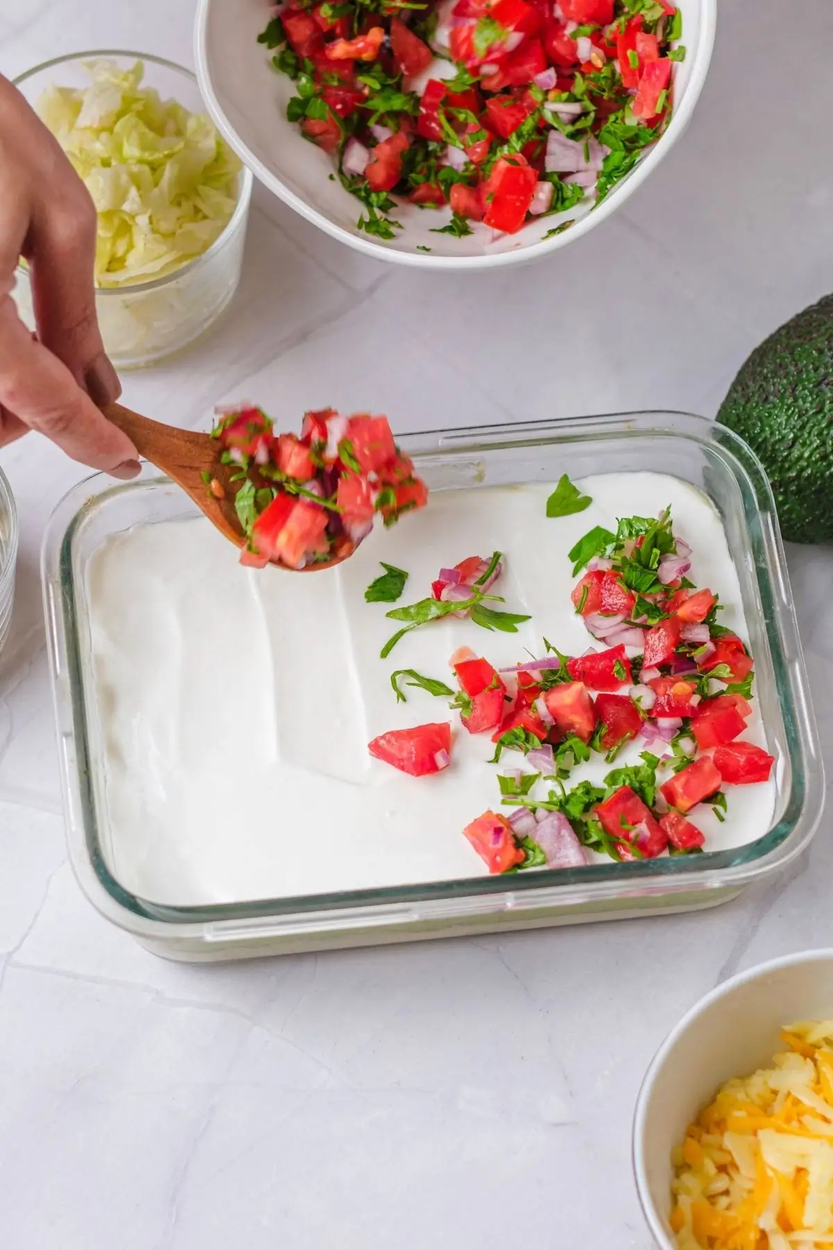 Spooning diced tomato, red onion and chopped arugula over the labneh layer