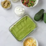 A smooth green avocado layer over hummus in a glass dish