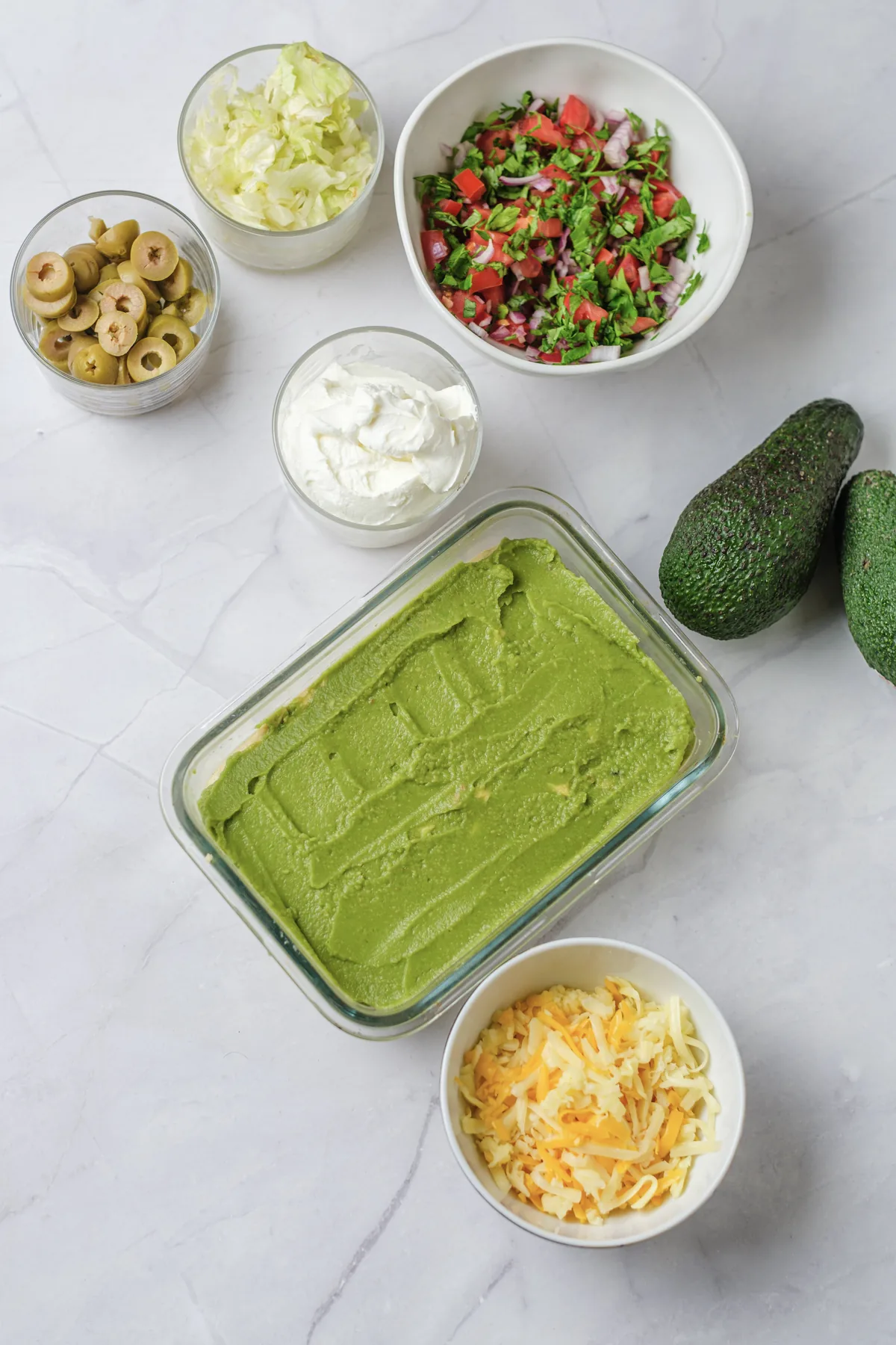 A smooth green avocado layer over hummus in a glass dish