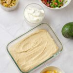 Hummus spread as the first layer of a vegetarian 7 layer dip in a glass dish