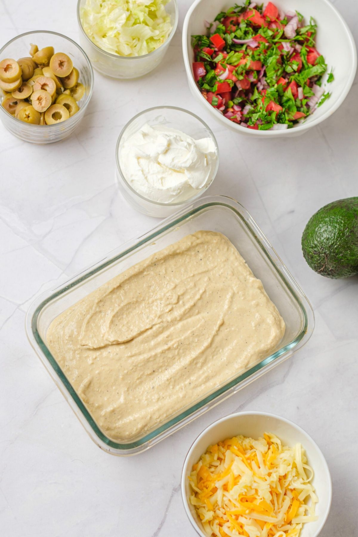 Hummus spread as the first layer of a vegetarian 7 layer dip in a glass dish