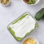A smooth white labneh layer spread over avocado in a glass dish
