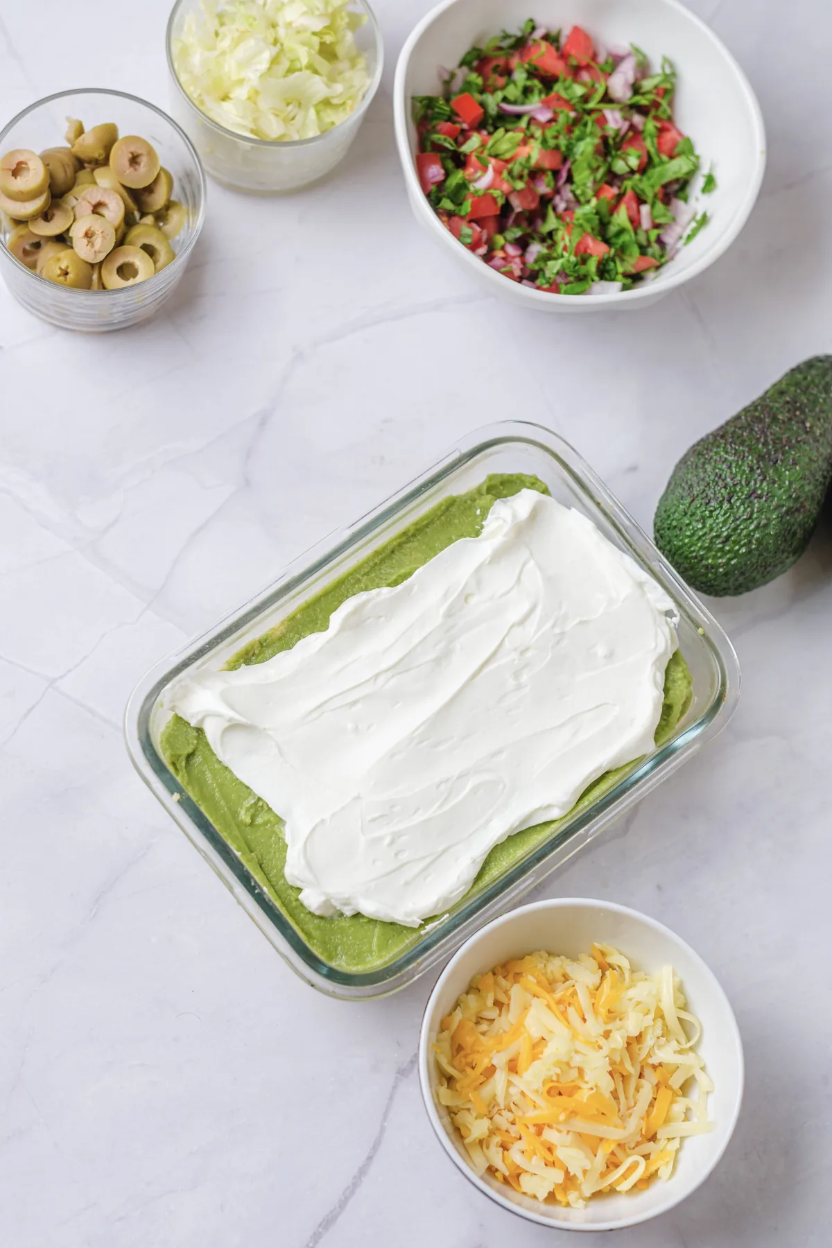 A smooth white labneh layer spread over avocado in a glass dish