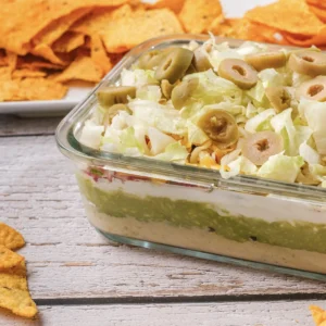 7 layer dip in a glass dish with tortilla chips